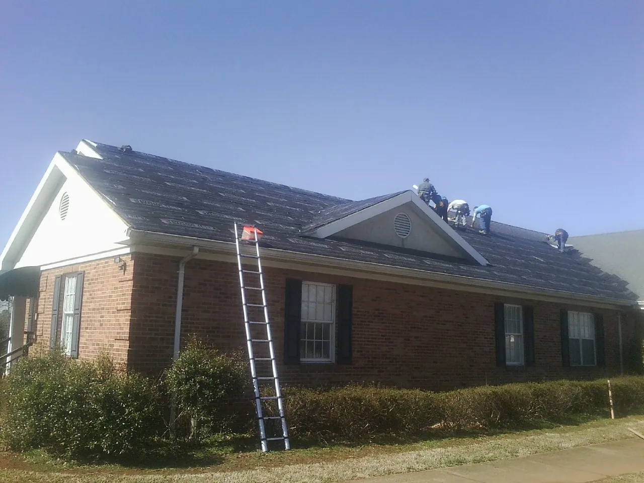 Crew tearing shingles off a brick ranch roof with a ladder set — Emergency Roof Repair work by our crew in Visalia