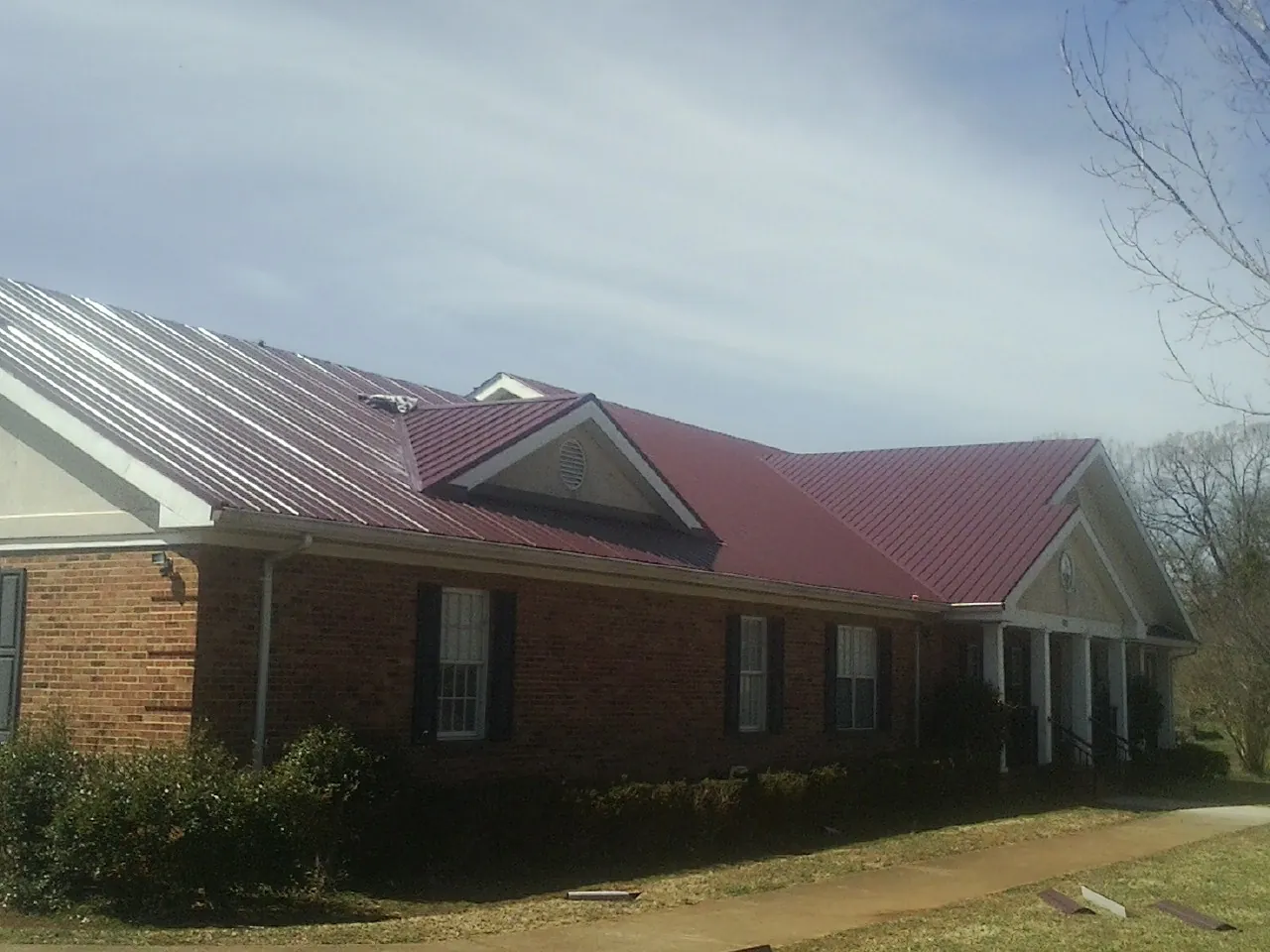 Red metal roof with gabled entries on a long brick building, from a Hail Damage Roof Repair job in Visalia