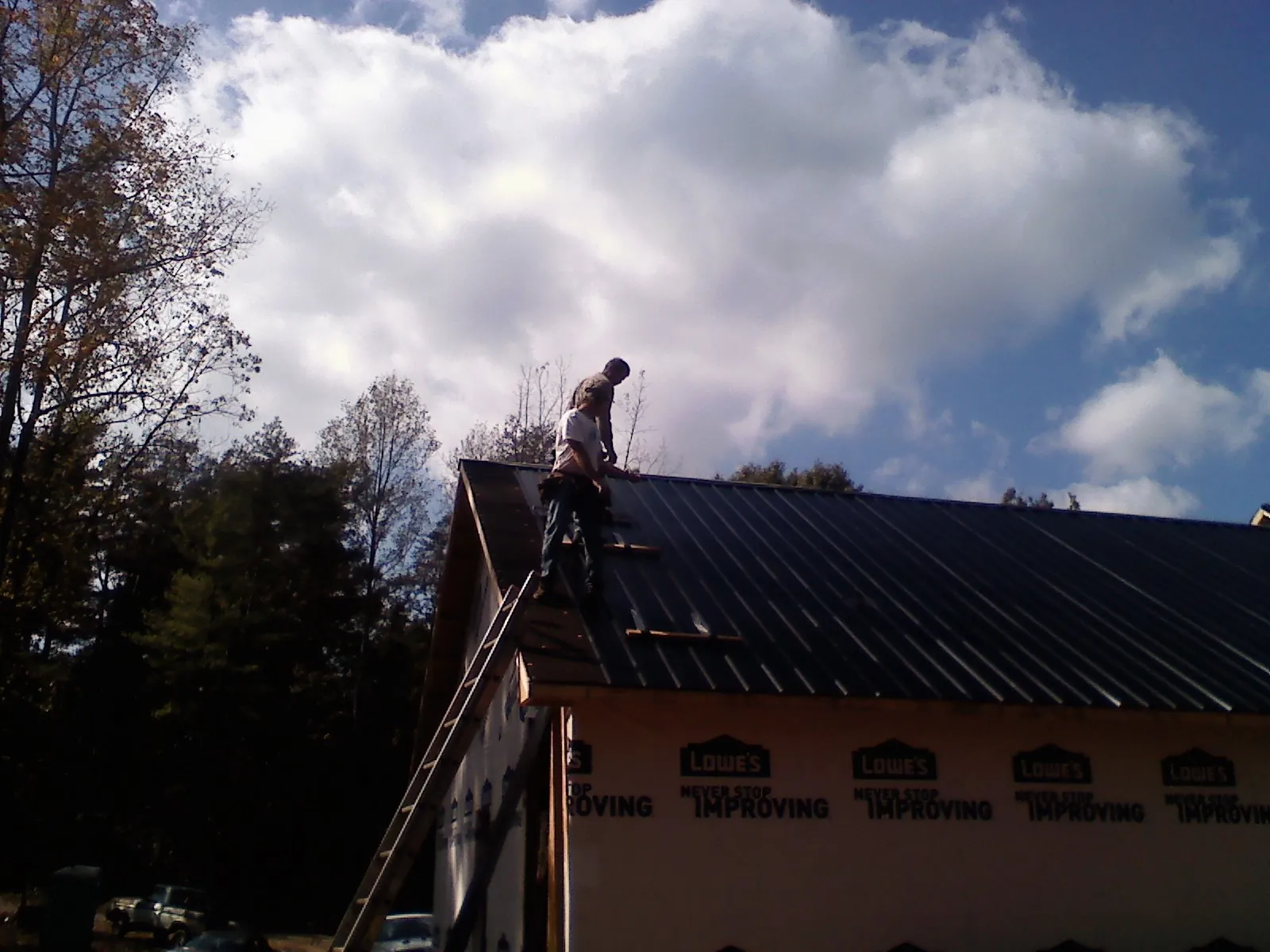 Roofer fastening dark metal panels high against a cloudy sky, from a Roof Inspection job in Visalia